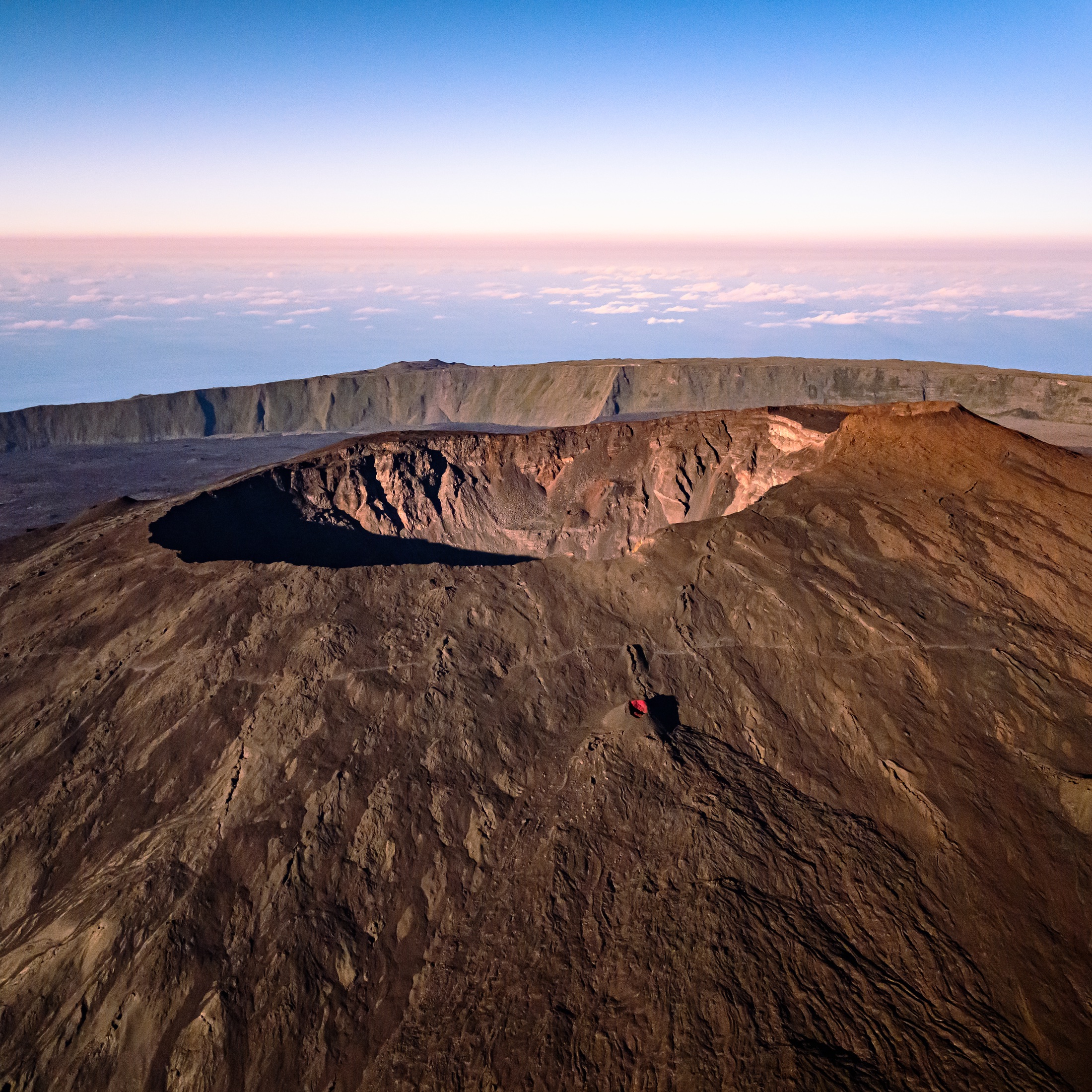 A broad volcanic crater in warm low-angle light above a layer of clouds on Réunion Island