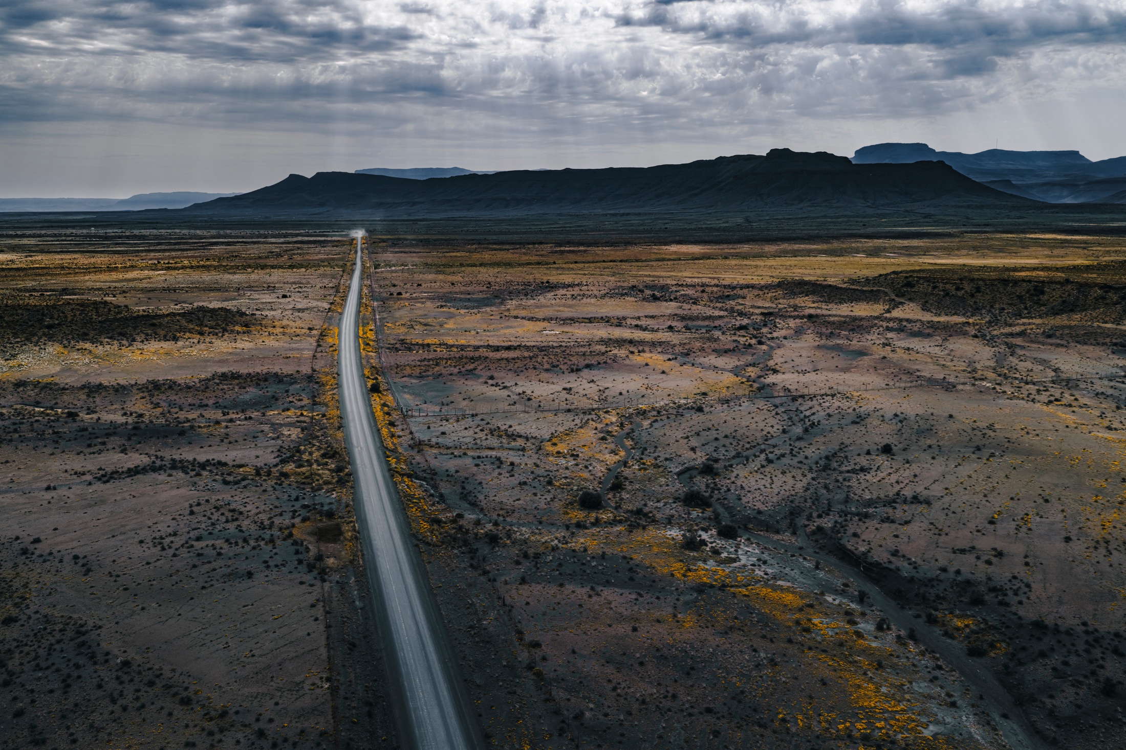 An aerial view of a long straight road crossing open Karoo country towards a dark mountain ridge